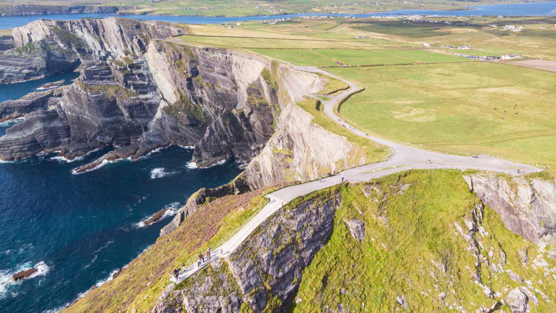Panoramic aerial view of the Kerry Cliffs, showcasing the dramatic meeting of lush green fields and rugged coastal cliffs in County Kerry, Ireland.