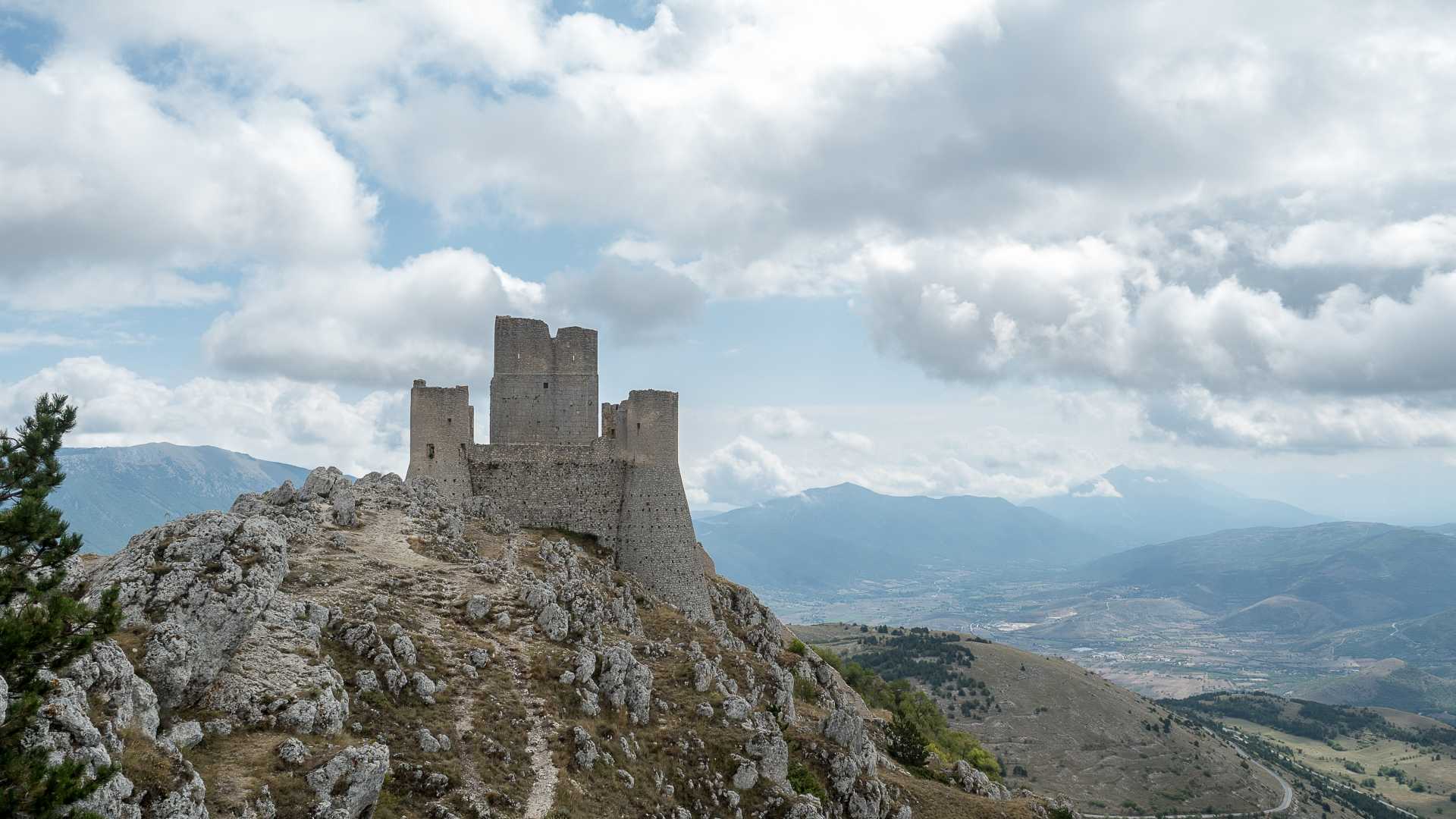 Rocca Calascio fortress crowns a rocky hill, surrounded by sweeping mountain views under a cloudy sky in Abruzzo, Italy.
