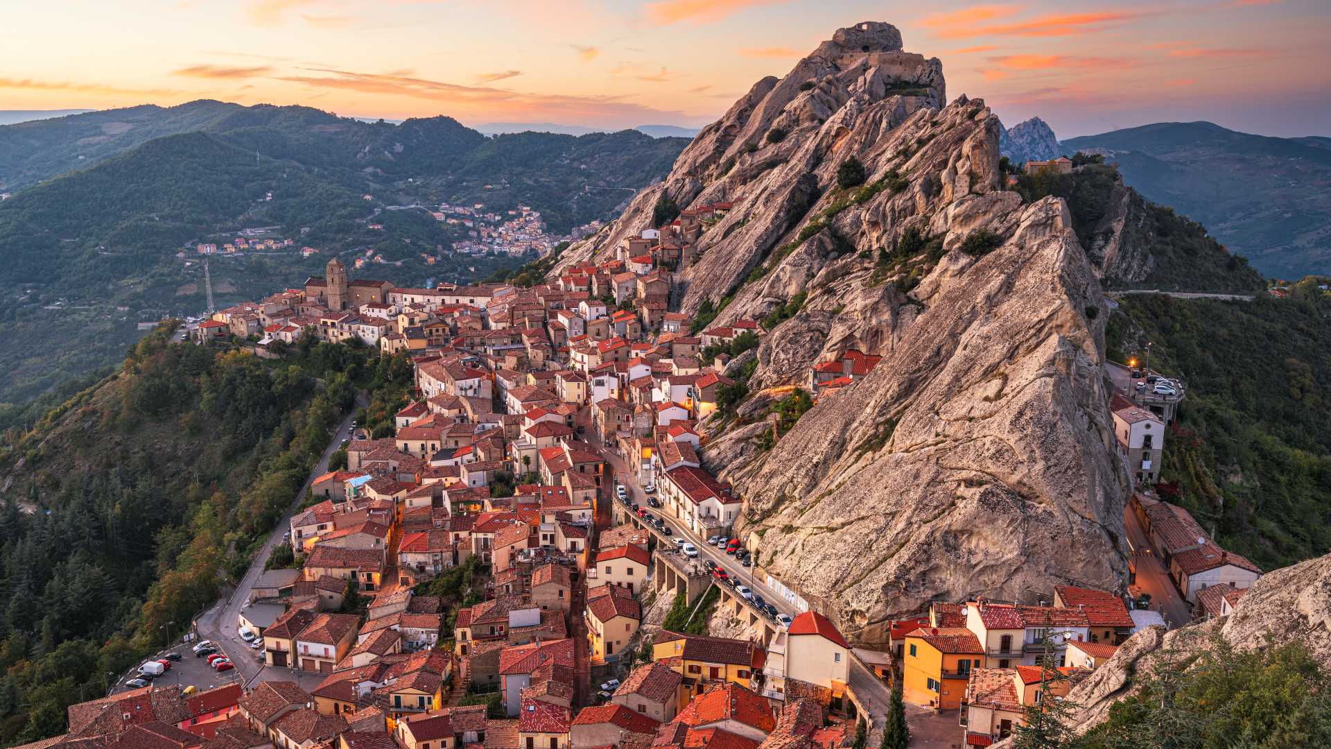 Pietrapertosa at dusk, a historic Italian village embraced by rugged cliffs, glowing warmly in the evening light.