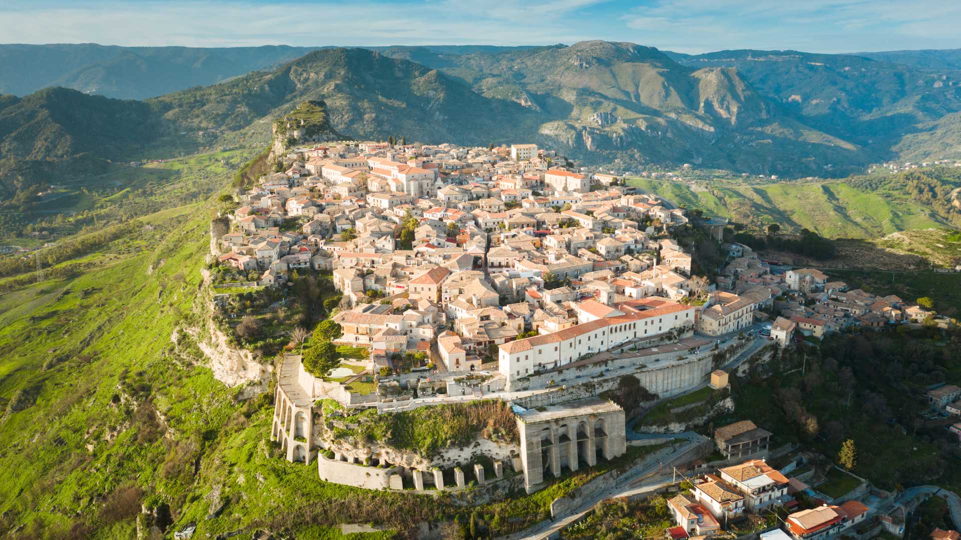 Gerace, Calabria: A medieval town with terracotta roofs and stone buildings, perched on a green hilltop.