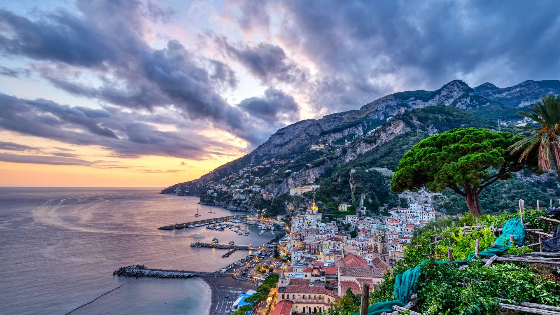 Amalfi's colorful houses cascade down to the coastline under a stunning sunset sky.