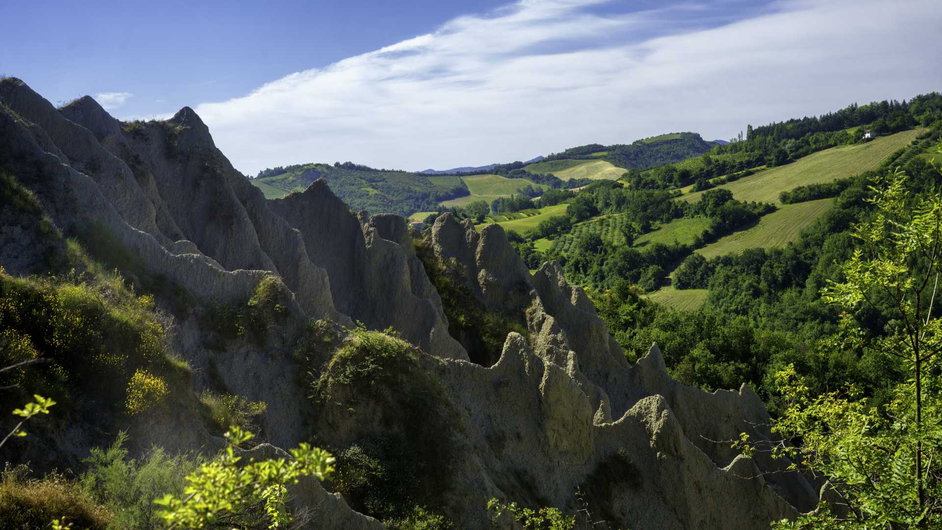 Rugged calanques rise amidst lush green hills near Imola, Italy, under a bright spring sky.