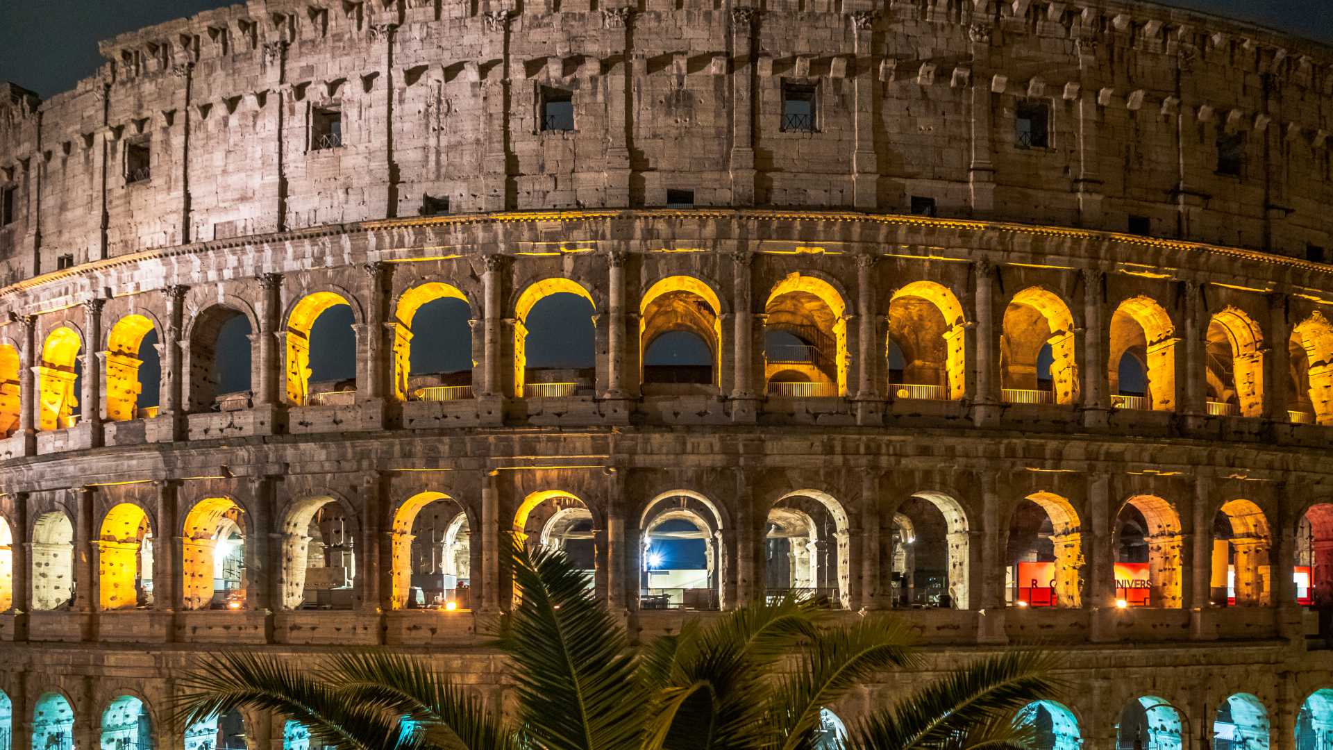 The Colosseum in Rome at night, showcasing its illuminated arches and ancient architecture.