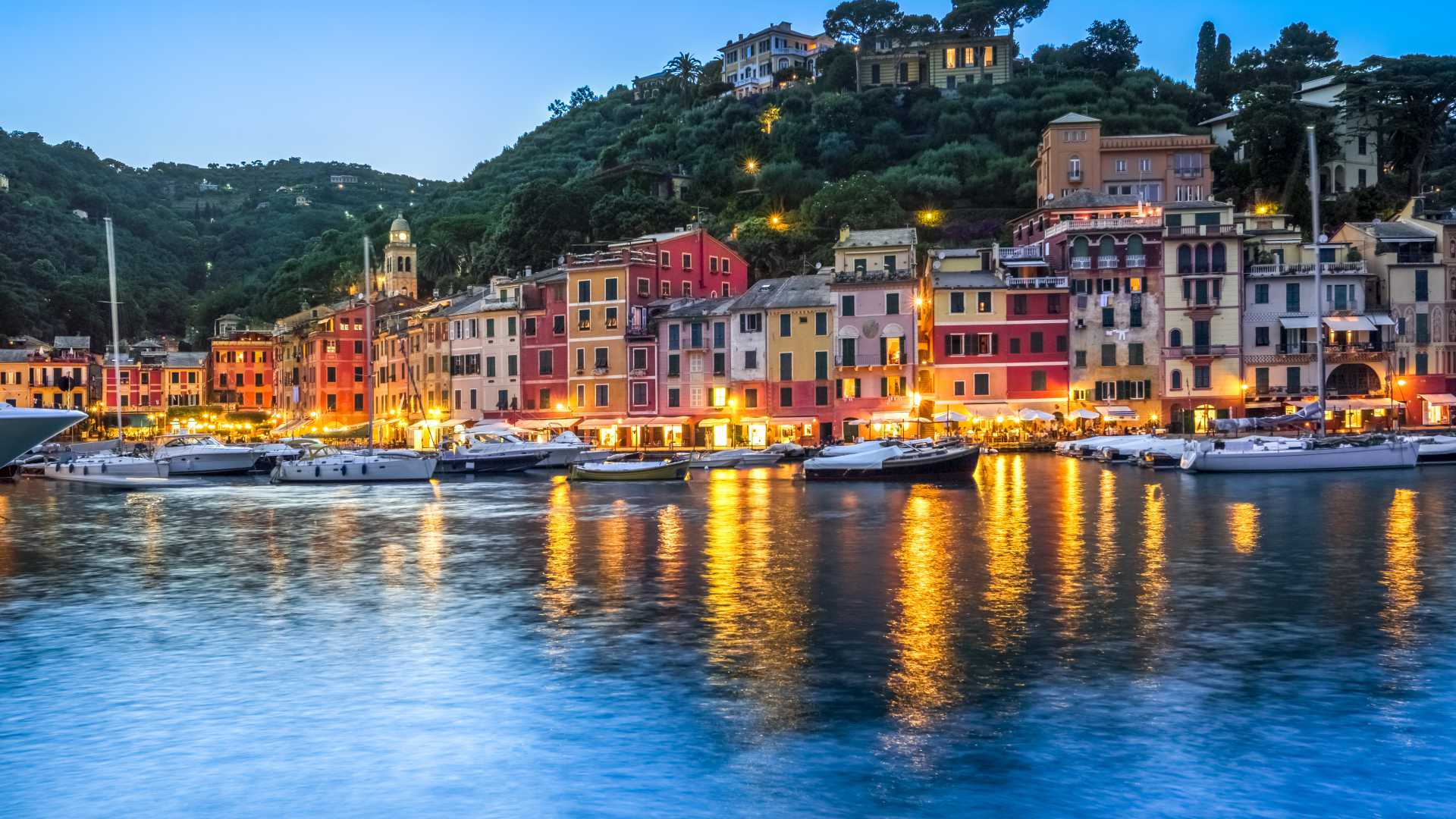Boats in Portofino's harbor reflect the village's lights at dusk.