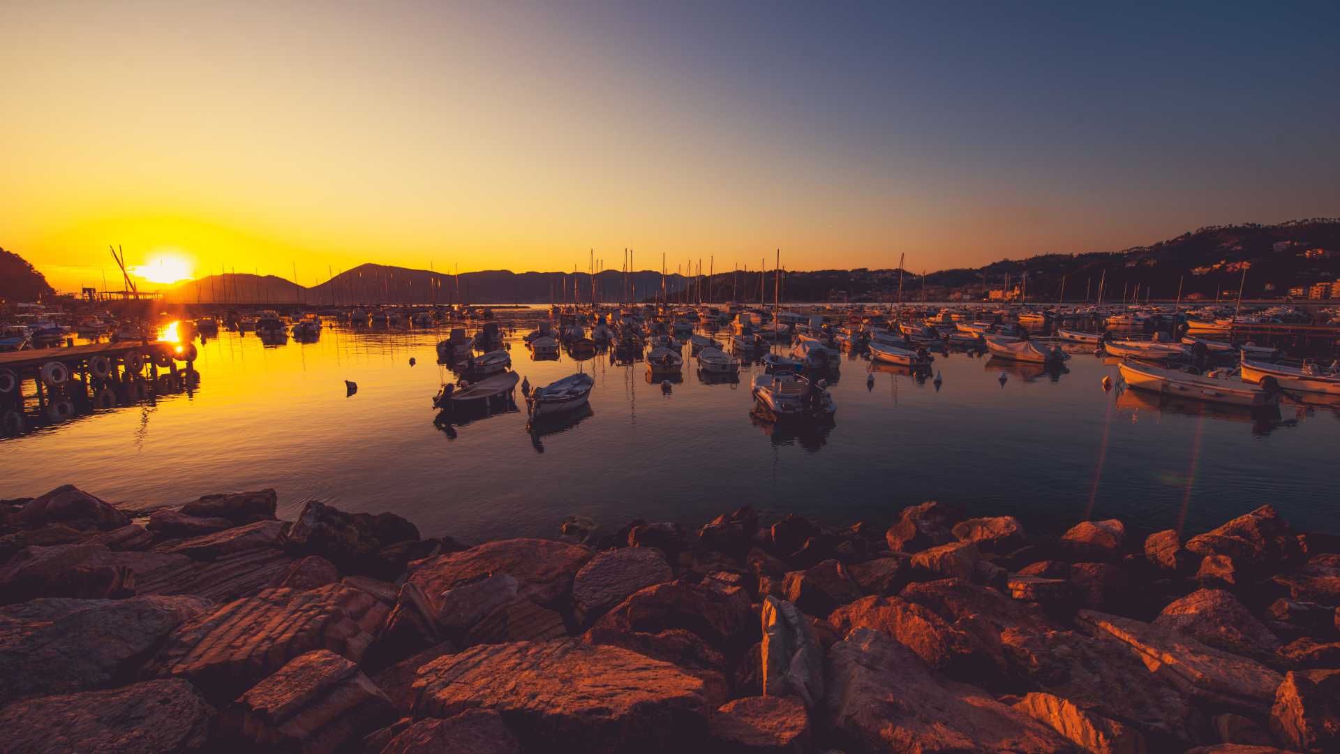 Sunset over Lerici Marina, with boats gently floating on the calm Mediterranean Sea, casting golden reflections.