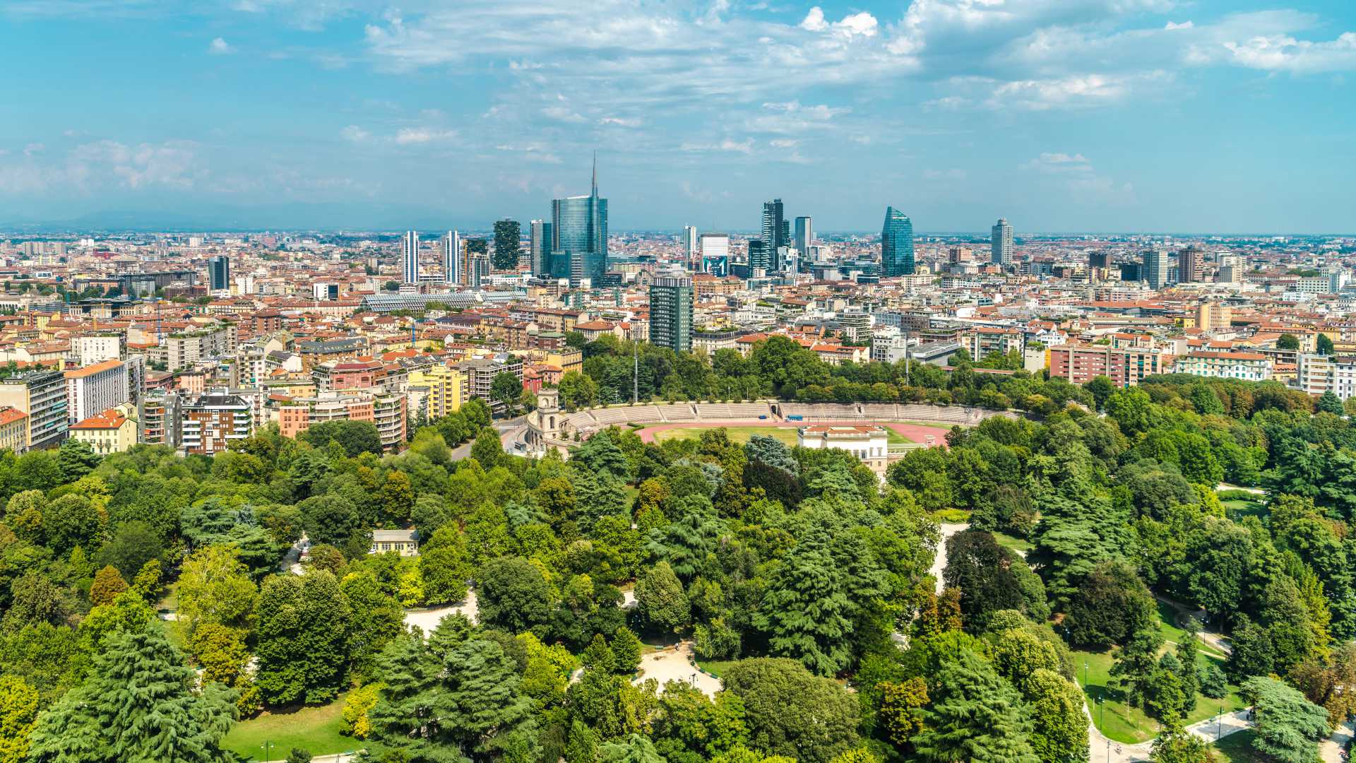 Panoramic view of Milan, showcasing modern skyscrapers and the green expanse of Parco Sempione under a sunny sky.