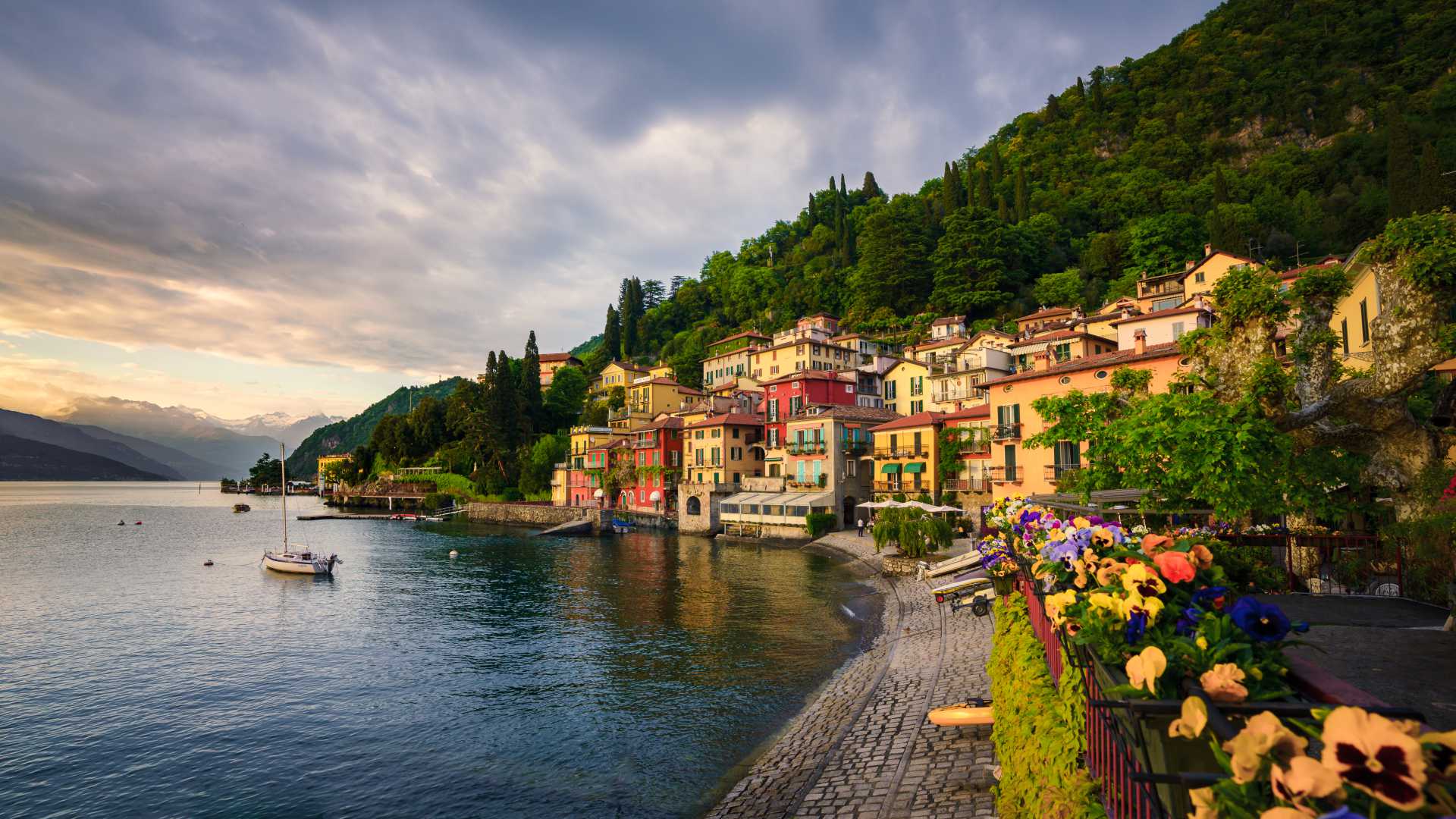 Colorful houses of Varenna line the shore of Lake Como, backed by lush hillsides at sunset.