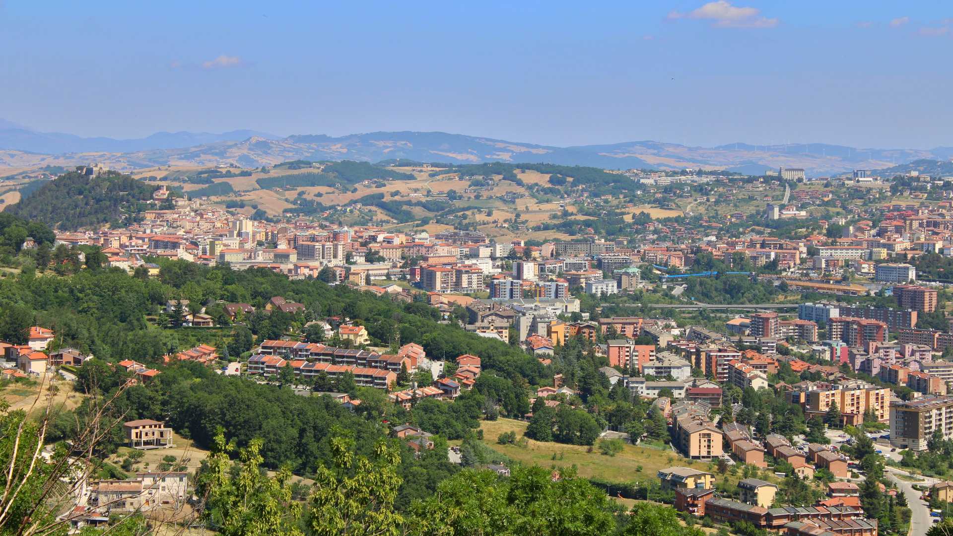 A panoramic view of Campobasso nestled among green hills under a clear blue sky.