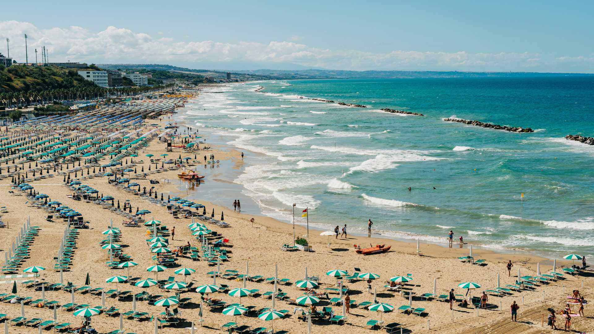 Crowded beach in Termoli, Italy, with rows of colorful umbrellas and turquoise waves under a sunny sky.