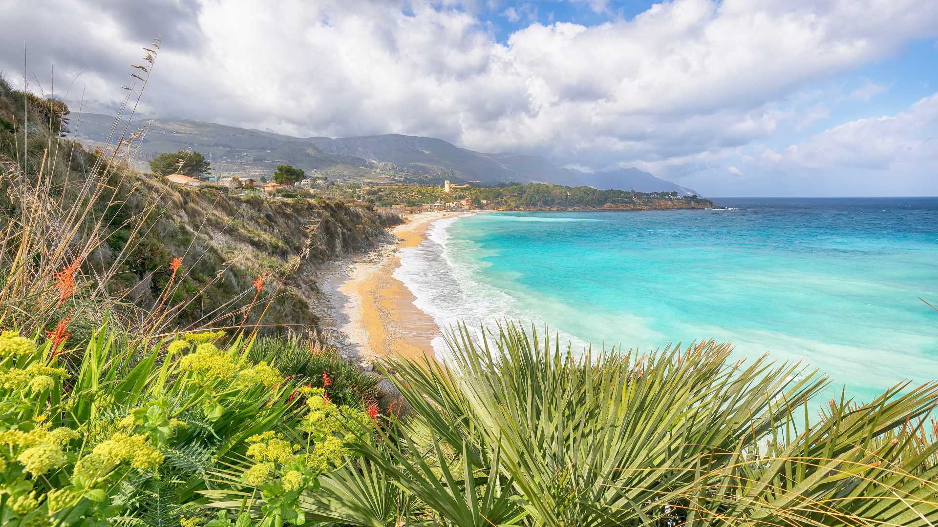 Azure sea and golden beach at Guidaloca, framed by greenery and cliffs.