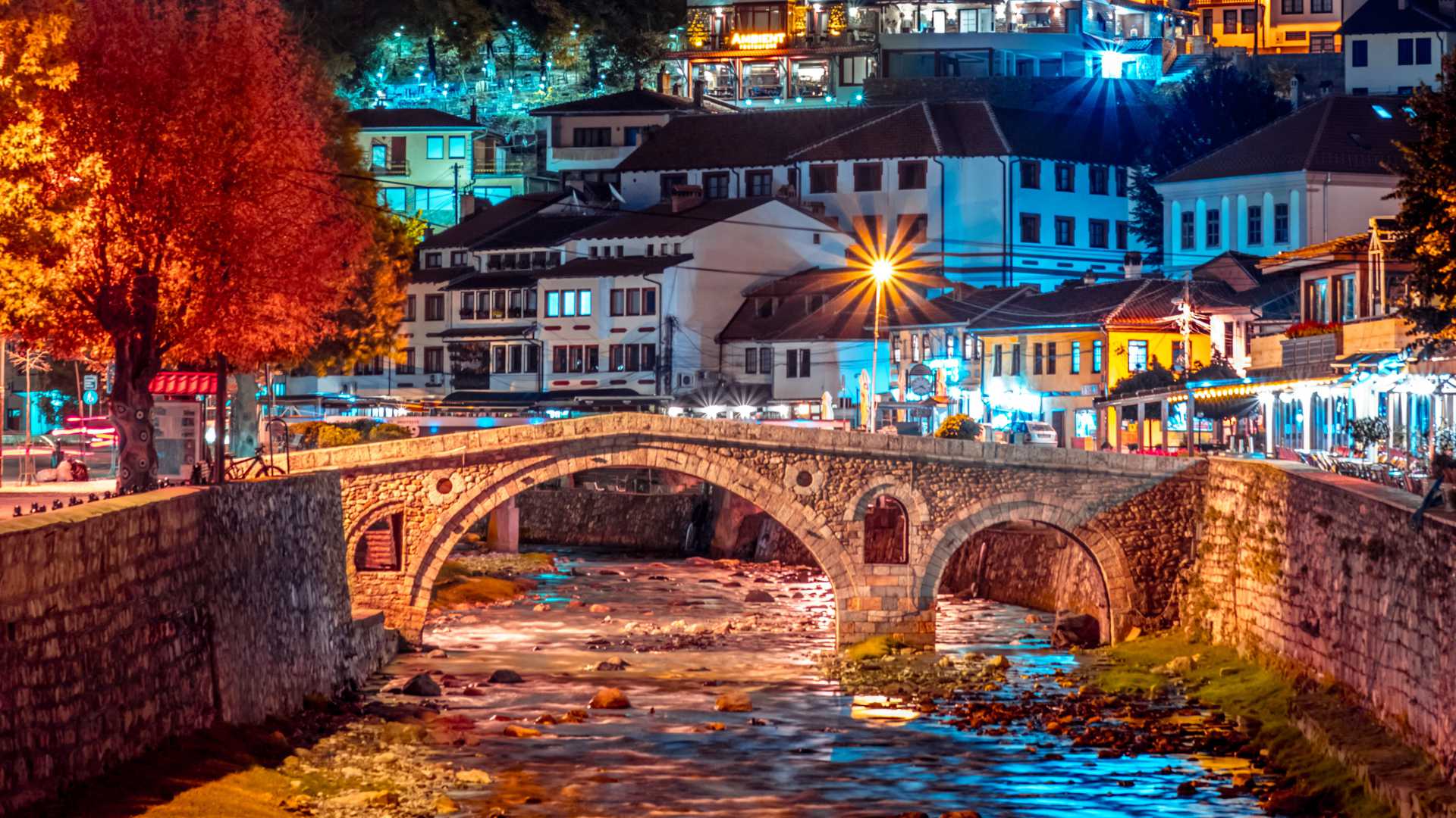 Vue nocturne du pont de pierre de Prizren, au Kosovo, avec des bâtiments illuminés le long de la rivière Lumbardhi.
