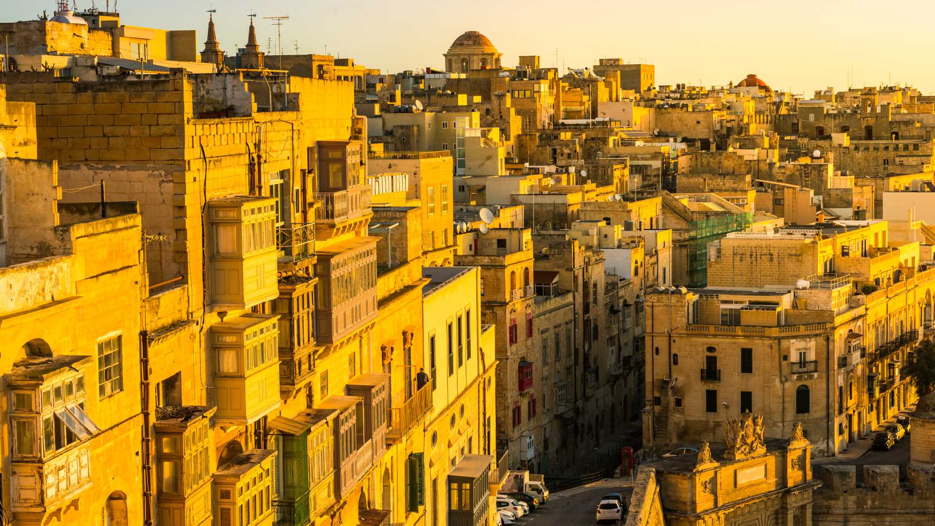 Golden sunrise bathes Valletta's historic buildings and enclosed balconies in warm morning light.