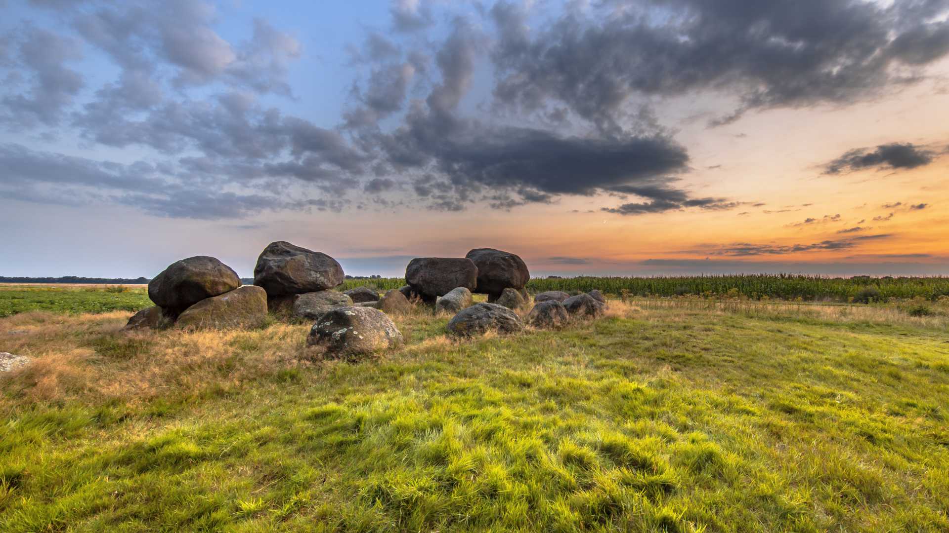 Oude hunebedstenen in een grasveld nabij Assen, Drenthe, onder een dramatische zonsonderganghemel.