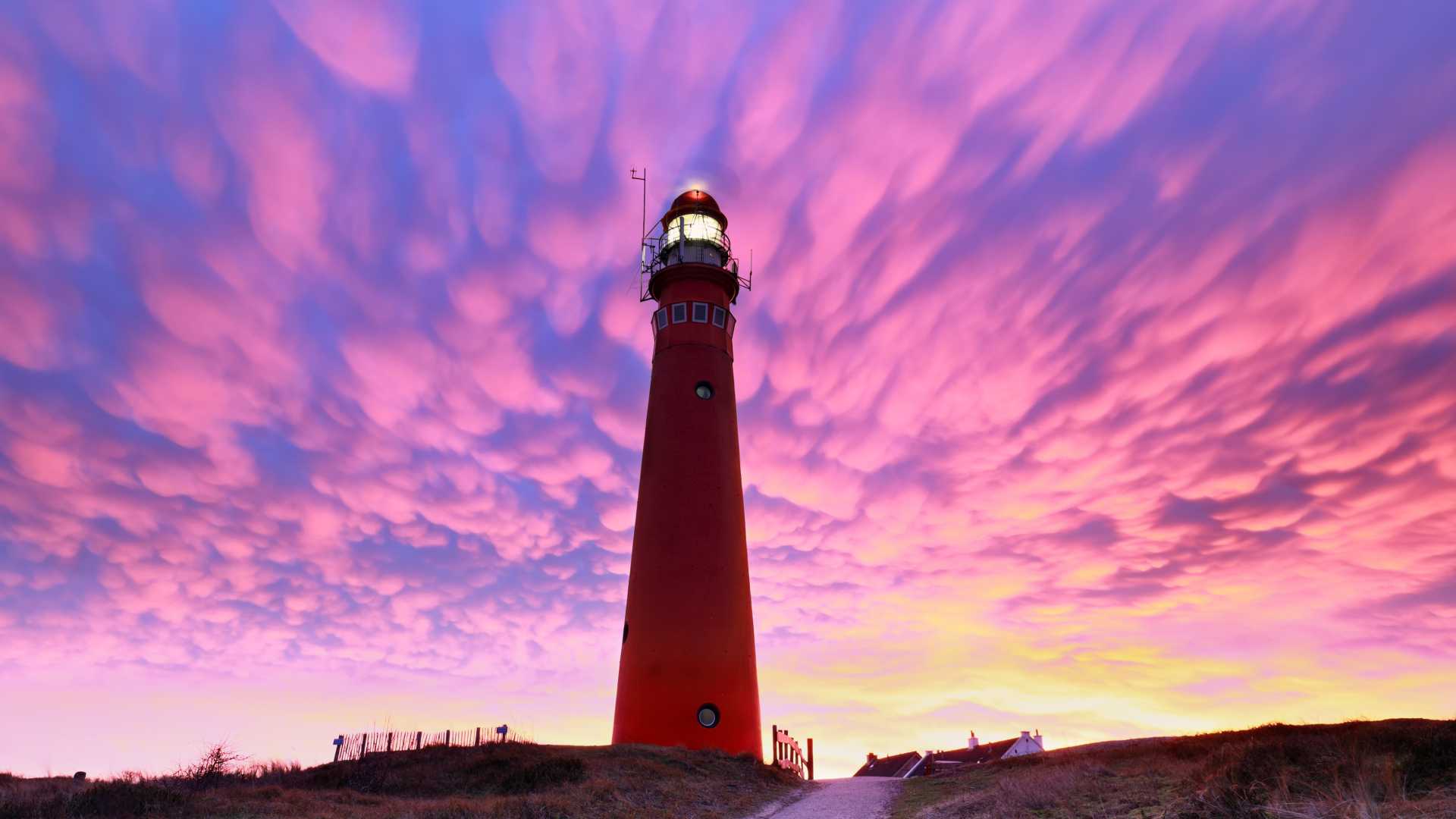 A red lighthouse stands beneath dramatic purple mammatus clouds on the island of Schiermonnikoog, Netherlands.