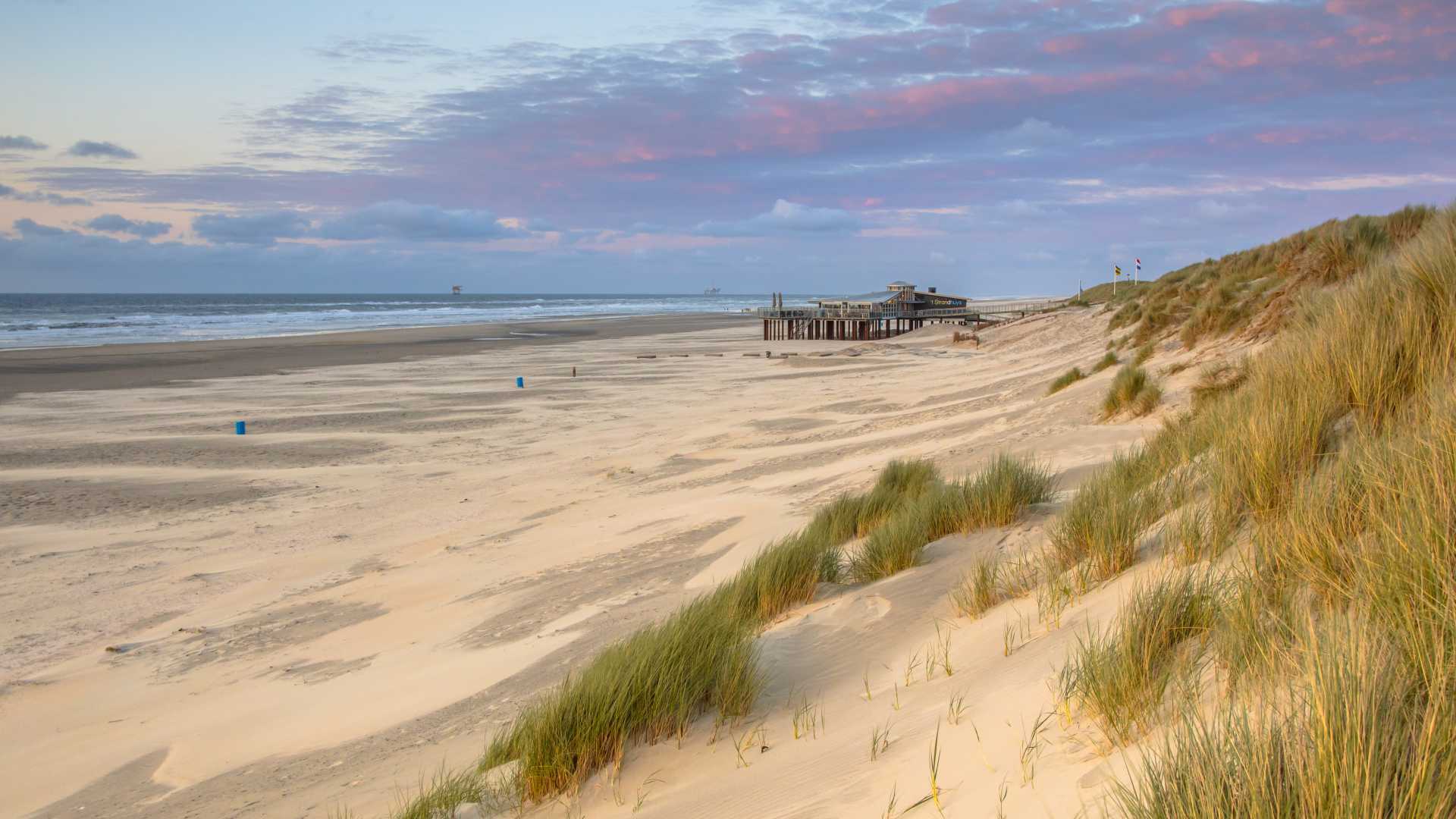 在阿梅兰岛的日落时分，覆盖着高高的草的沙丘俯瞰着宁静的北海。