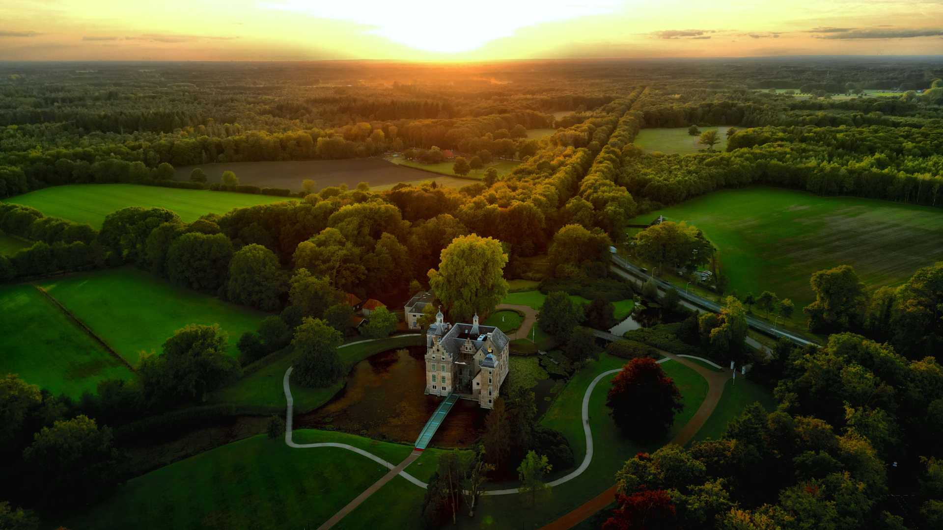 Luchtfoto van kasteel Ruurlo, badend in gouden zonlicht, omgeven door een groen landschap in Gelderland, Nederland.