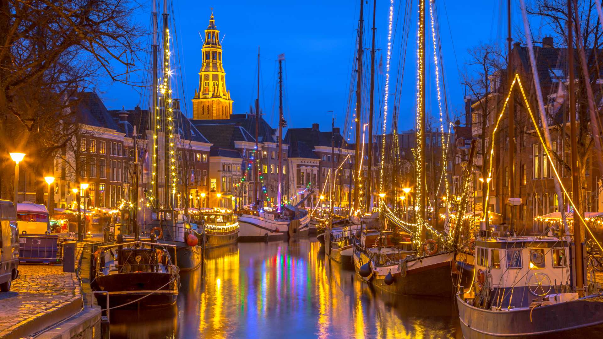 Voiliers historiques illuminés de manière festive amarrés le long du quai Hoge der Aa à Groningen pendant le festival Winterwelvaart.