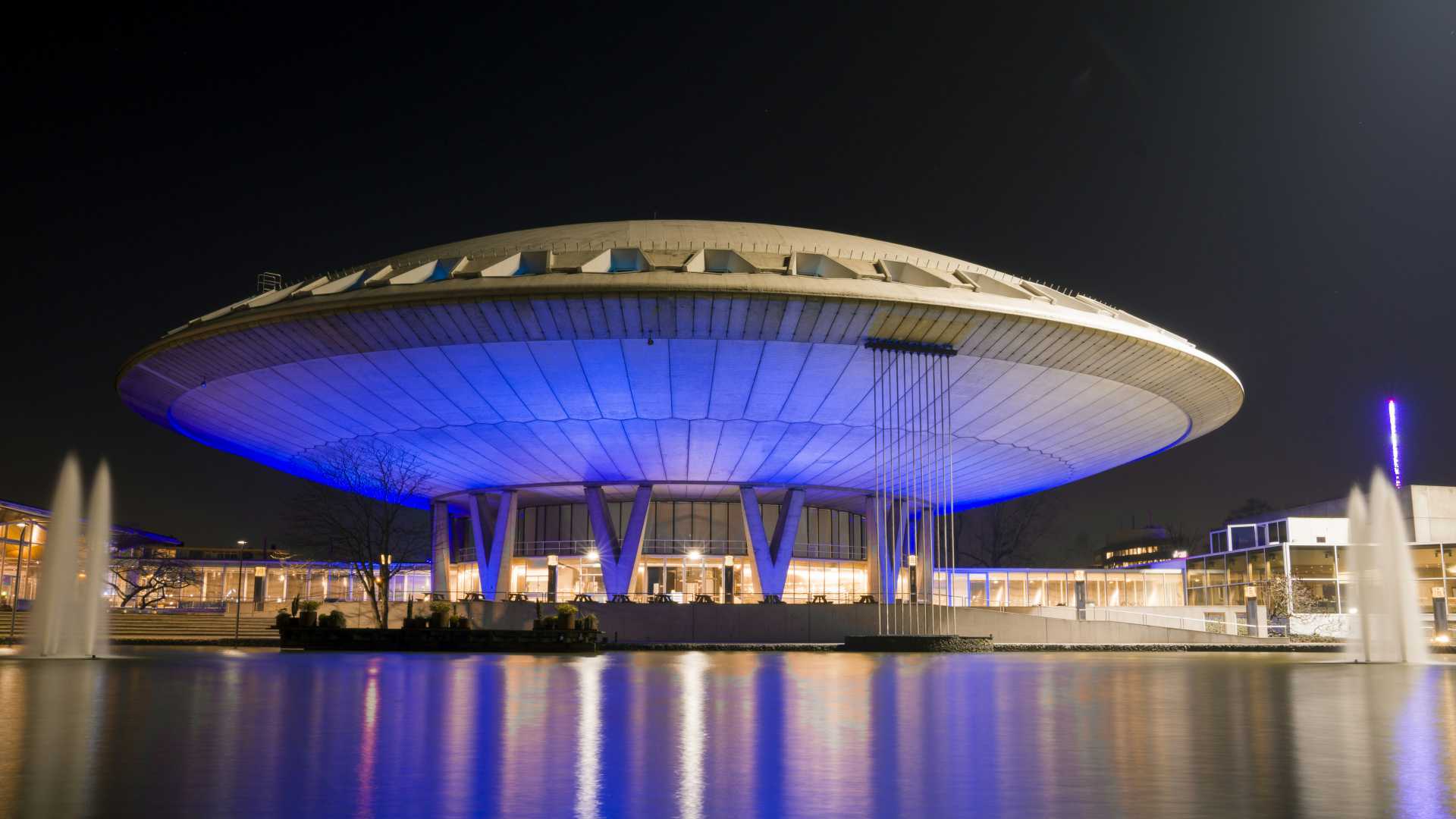 De Evoluon in Eindhoven, Nederland, 's nachts verlicht, weerspiegeld in het water.