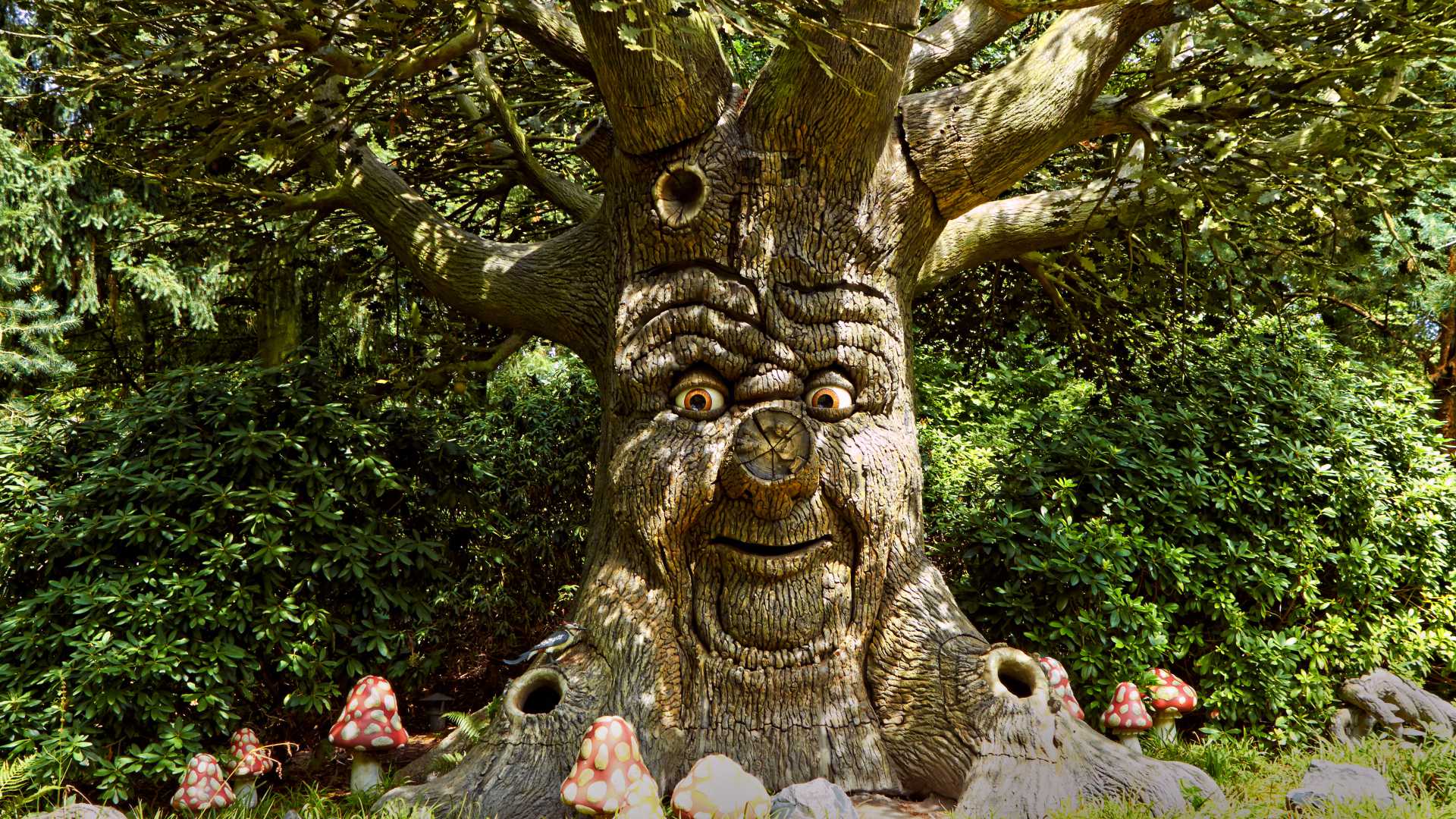 Ein skurriler sprechender Baum mit einem freundlichen Gesicht, umgeben von üppigem Grün und Krötenstühlen in Efteling.