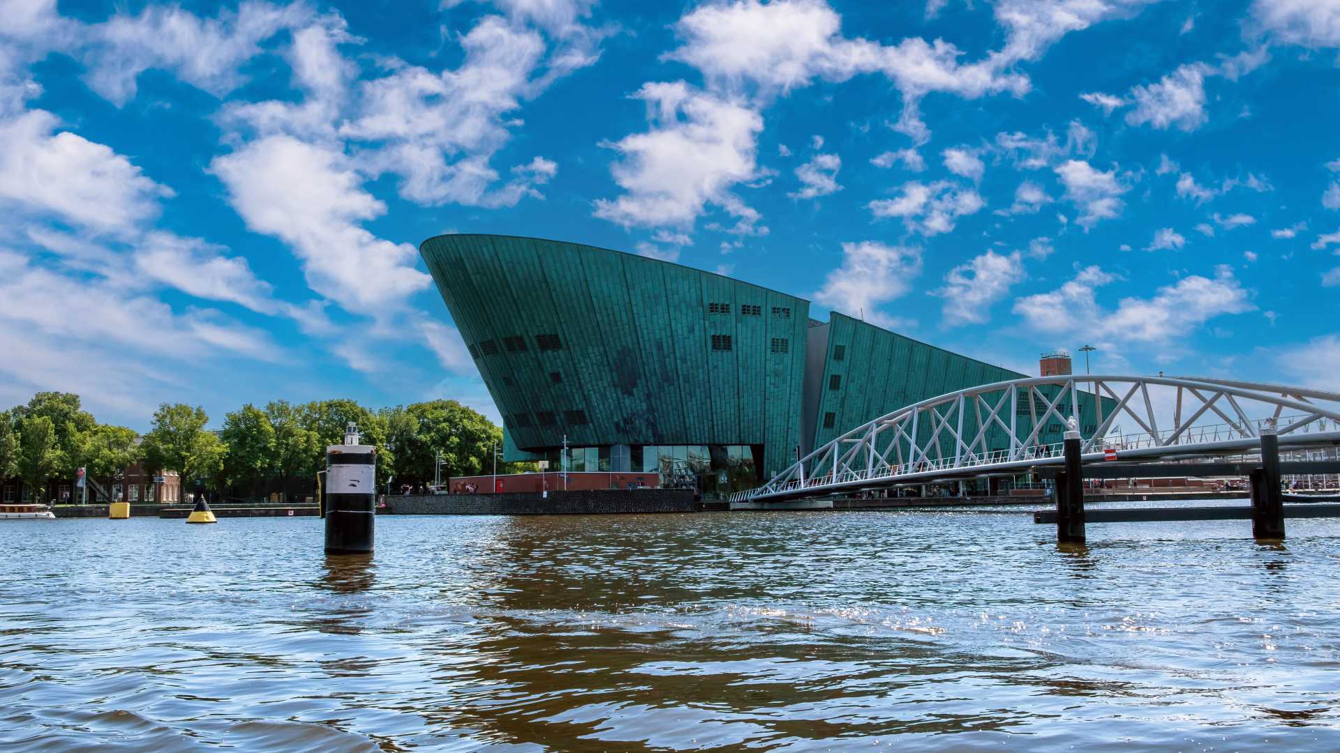 NEMO Science Museum's distinctive ship-like green structure stands by the waterfront under a vibrant blue sky in Amsterdam.