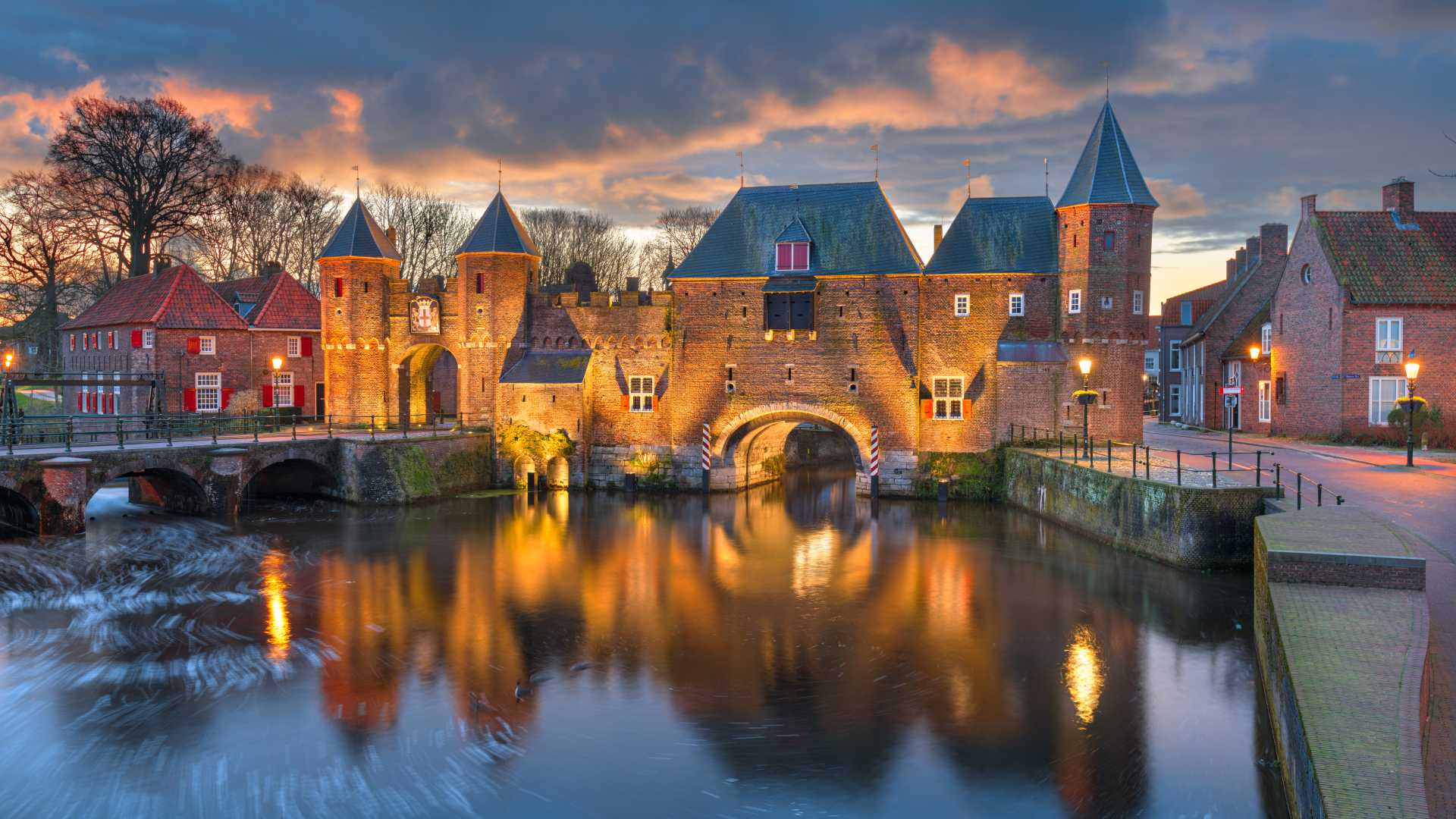 The historic Koppelpoort in Amersfoort, Netherlands, glows warmly at dawn, reflected in the tranquil waters below.