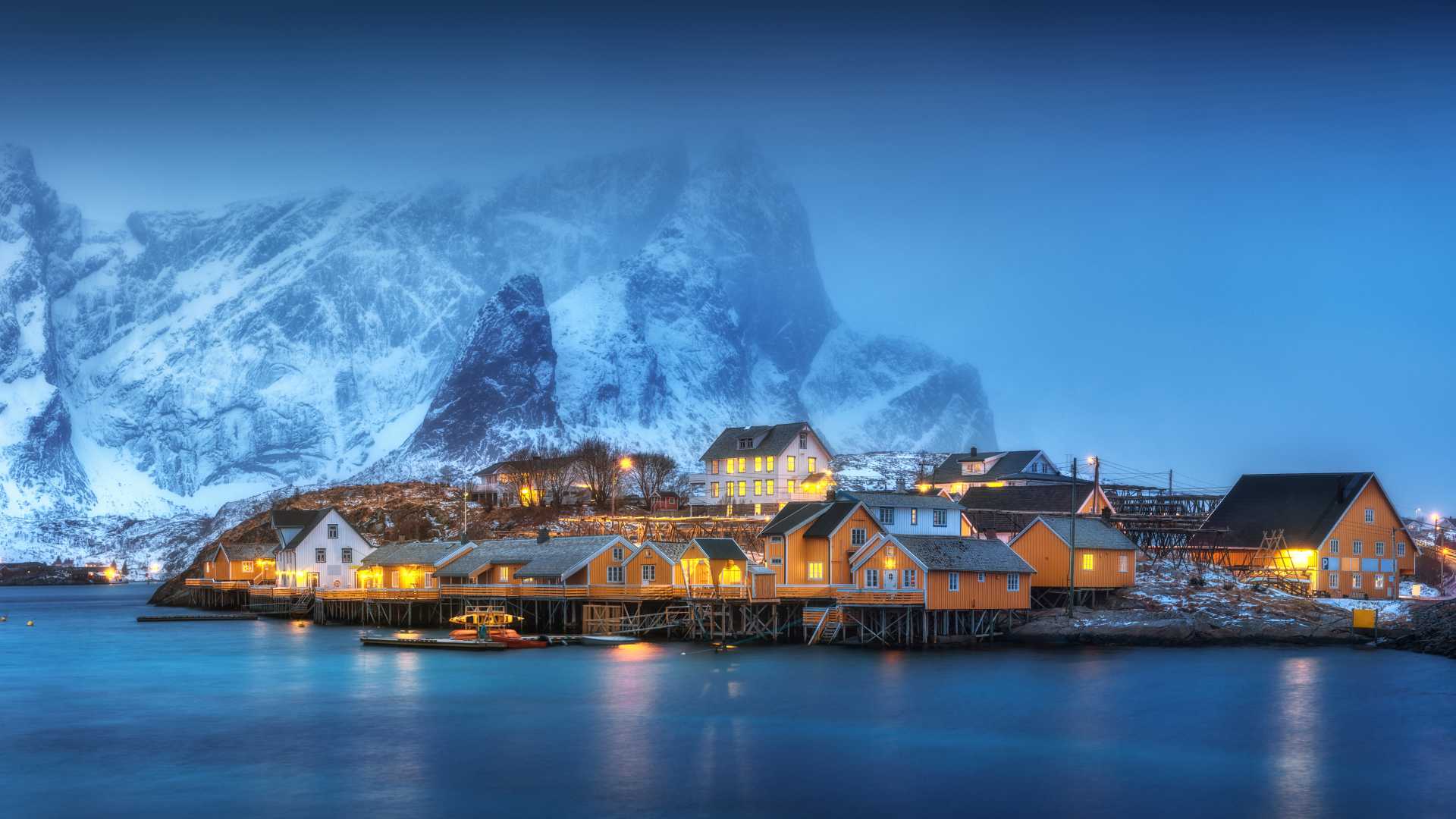 Los rorbuers amarillos brillan cálidamente en la noche de invierno, enclavados contra montañas nevadas en Lofoten, Noruega.