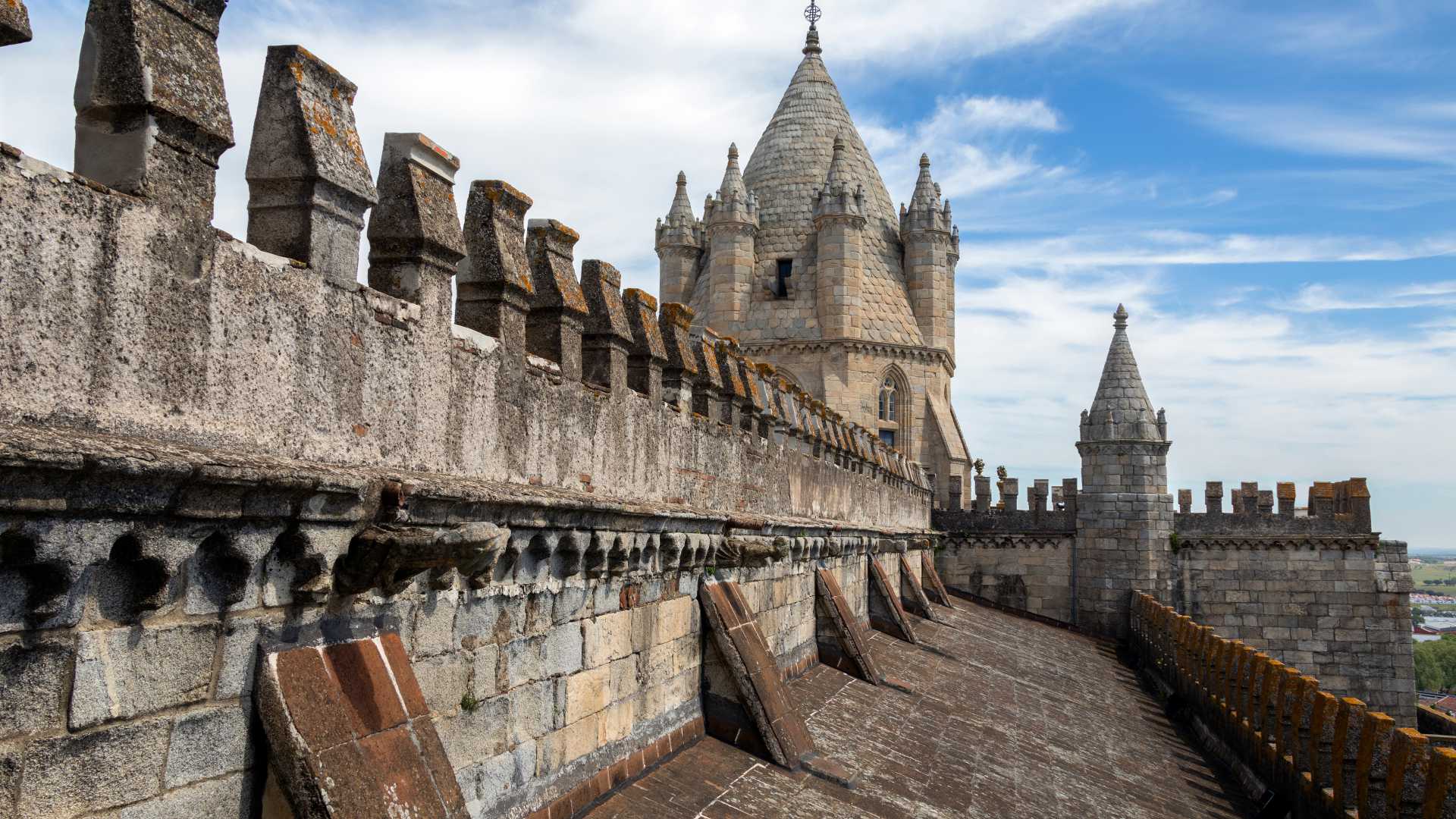 맑은 푸른 하늘을 배경으로 에보라 대성당 지붕의 돌탑과 첨탑이 중세 건축 양식을 보여줍니다.