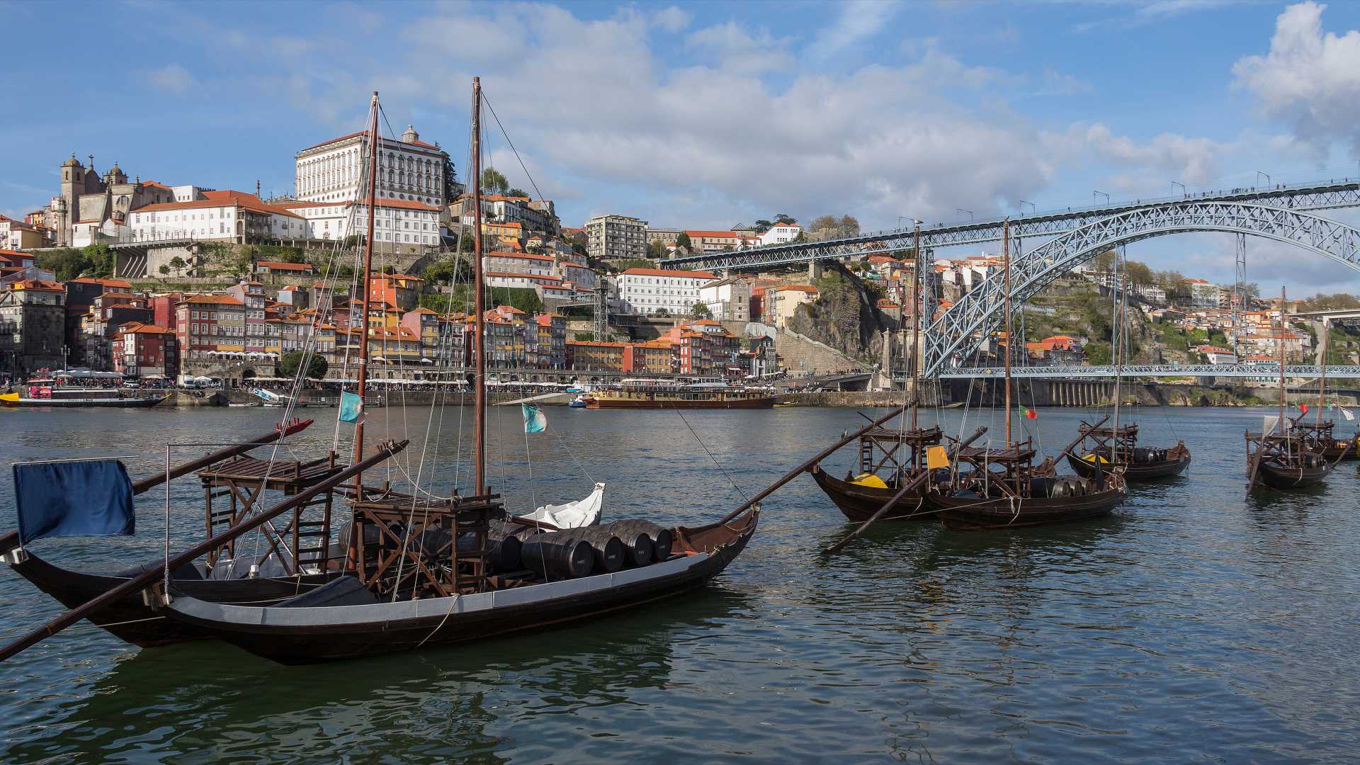 Traditionele boten op de Douro-rivier, met de historische gebouwen van Porto en de Dom Luís I-brug op de achtergrond.