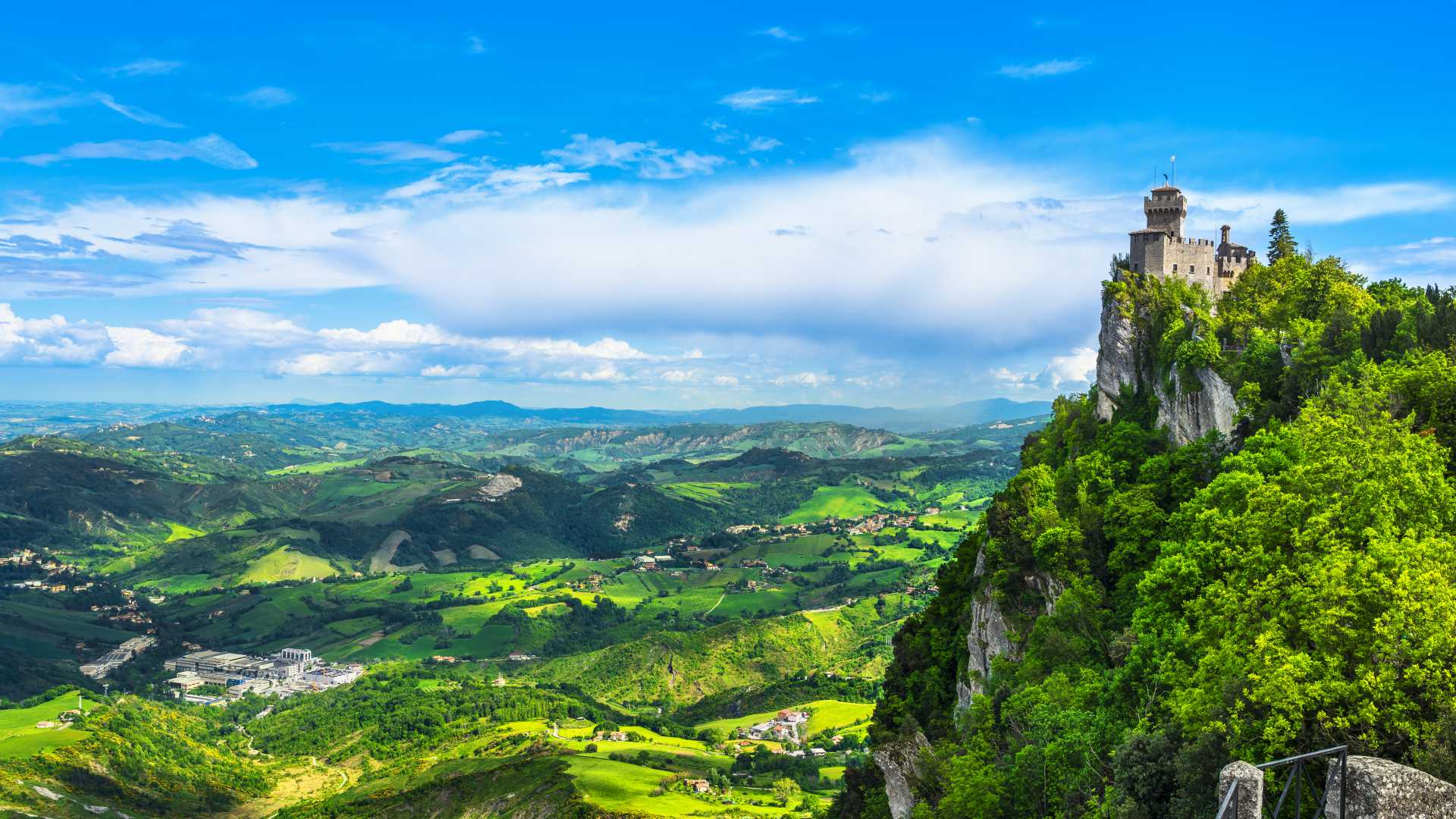 A medieval tower in San Marino stands on a rocky cliff, overlooking the scenic Romagna region.