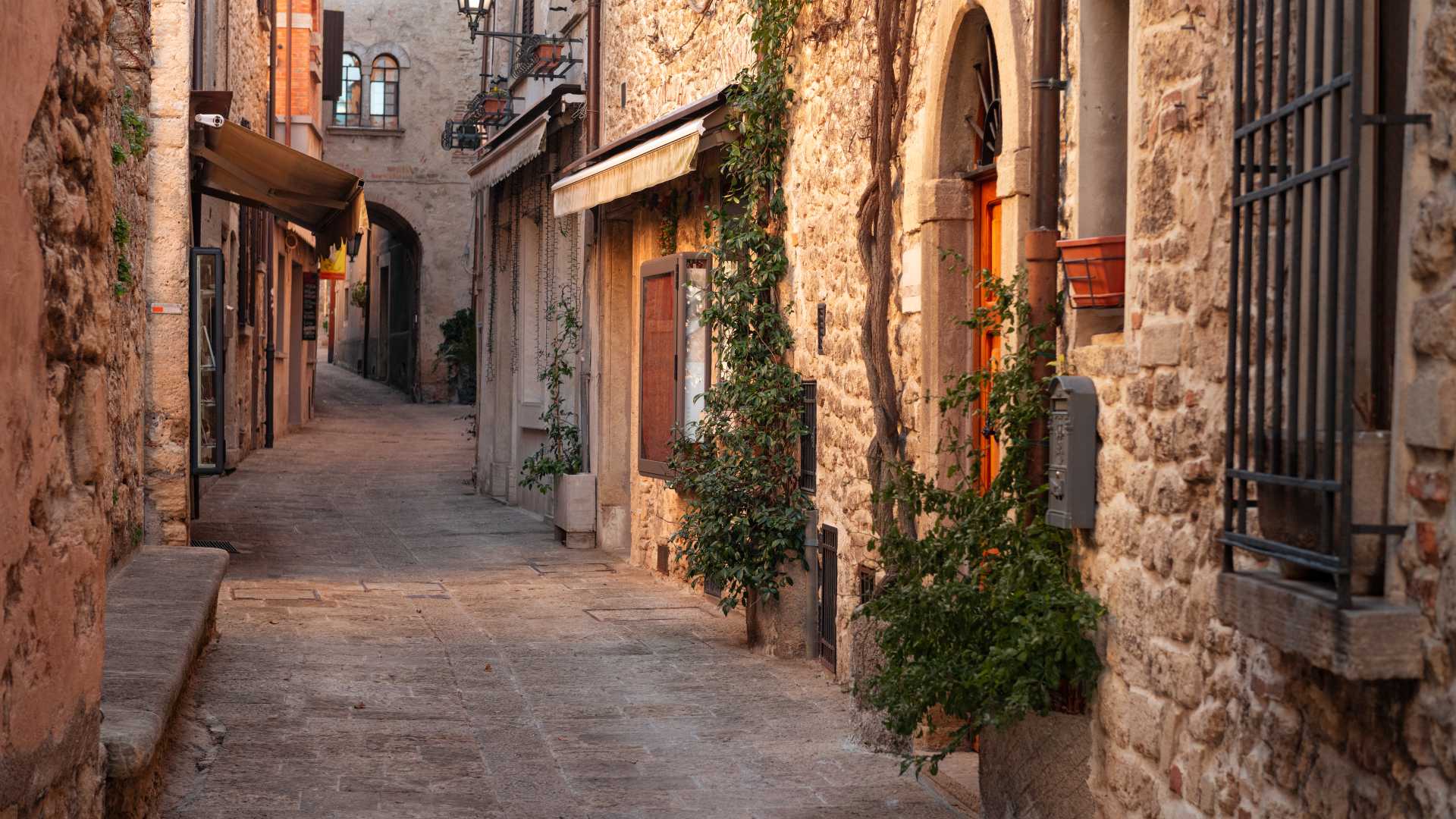 A picturesque, narrow alleyway in San Marino, featuring historic stone buildings and lush plants.