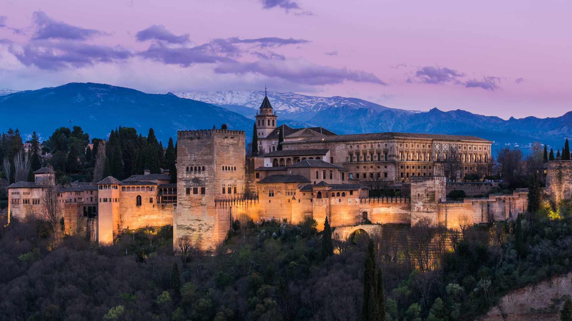 Het Alhambra paleis in Granada gloeit tegen een schemerende hemel, met de Sierra Nevada in de verte.