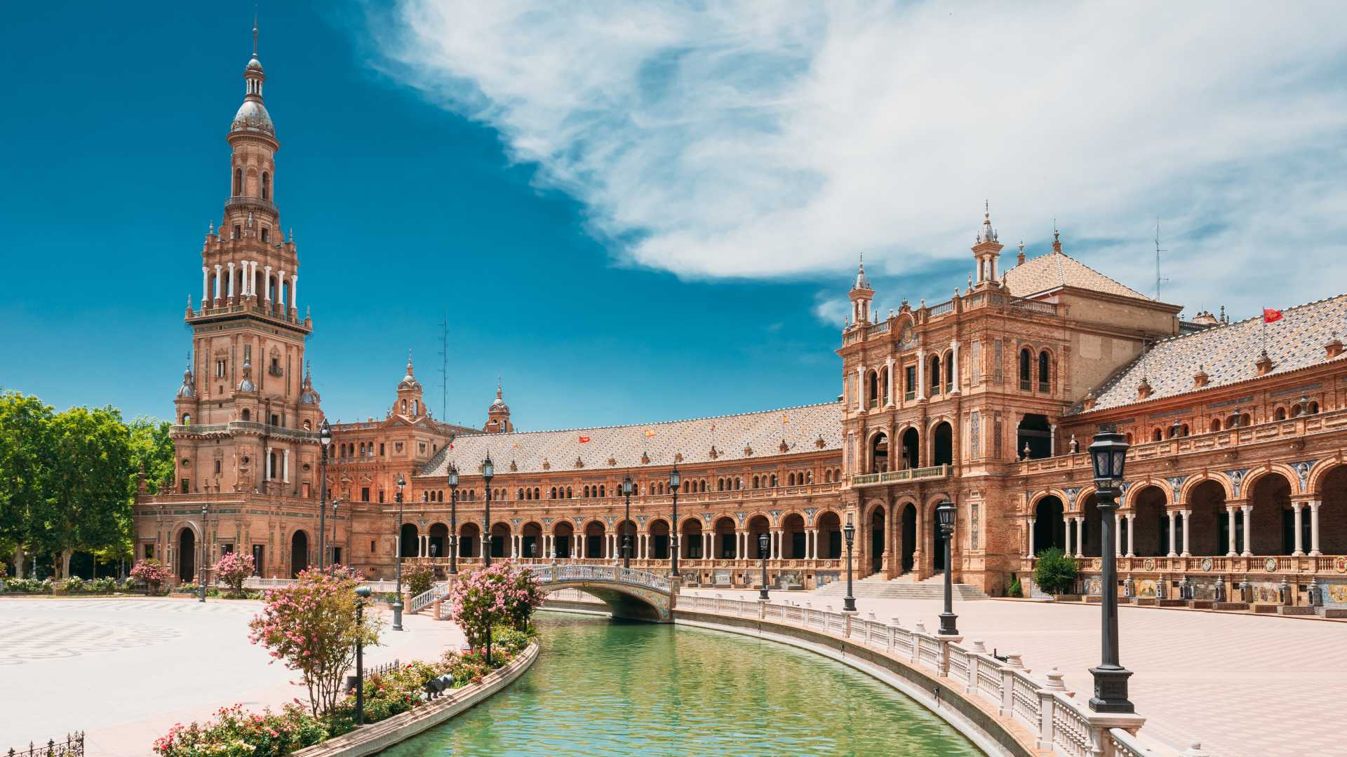 Renaissance Revival architectuur van Plaza de España in Sevilla met een serene gracht onder een helderblauwe hemel.