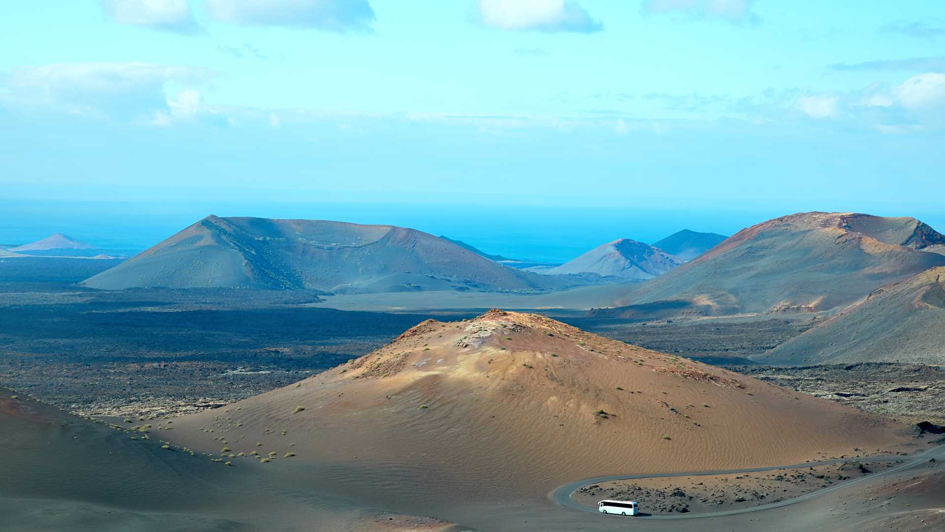 Panoramisch uitzicht op het vulkanische terrein van Nationaal Park Timanfaya in Lanzarote, met een touringcar op de weg.