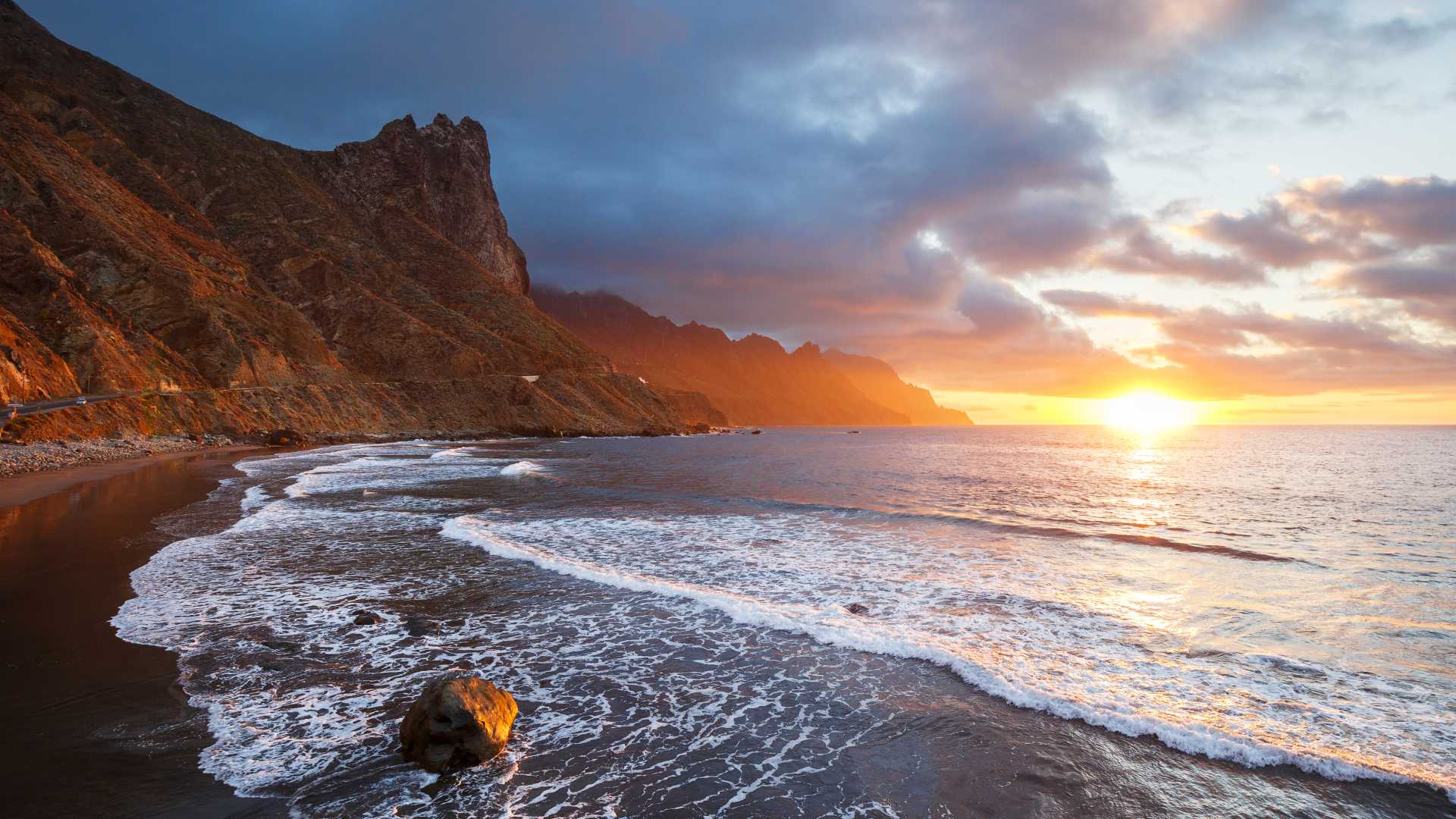 Gouden zonsondergang boven het zwarte vulkanische strand van Tenerife, met ruige kliffen en golven.
