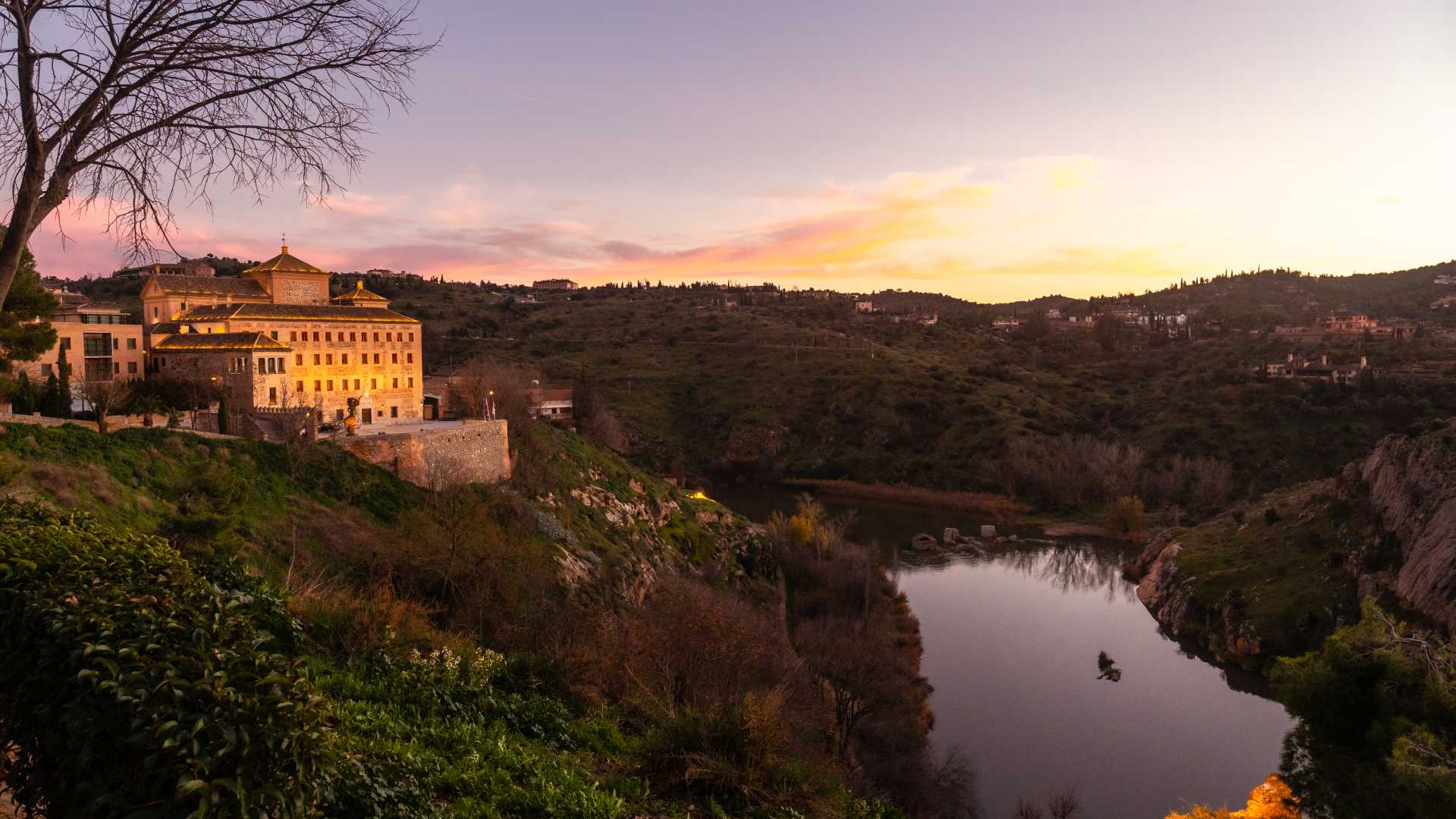 Sunset view of Toledo, Spain, with a golden glow over the city and the Tagus River.