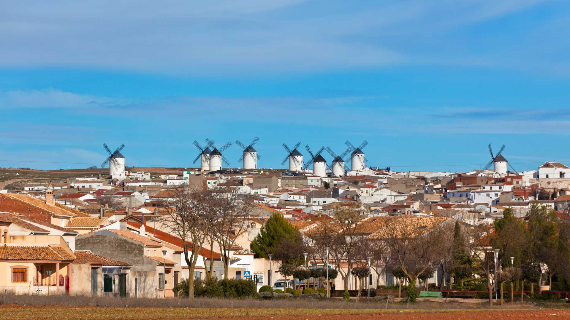 White windmills with four blades stand on a hill overlooking the town of Campo de Criptana, Spain.