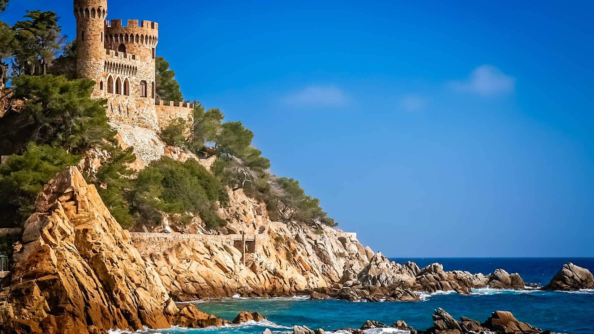 Kasteel Sant Joan staat trots op de rotsachtige kust van de Costa Brava, omgeven door de blauwe zee en weelderig groen.