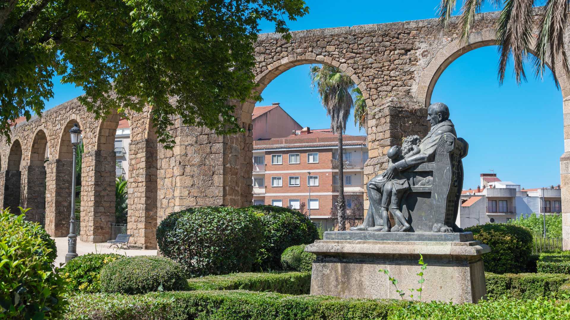 Bogen van het oude Romeinse aquaduct en standbeeld van de markies van Constancia in een weelderig park, Plasencia, Spanje.