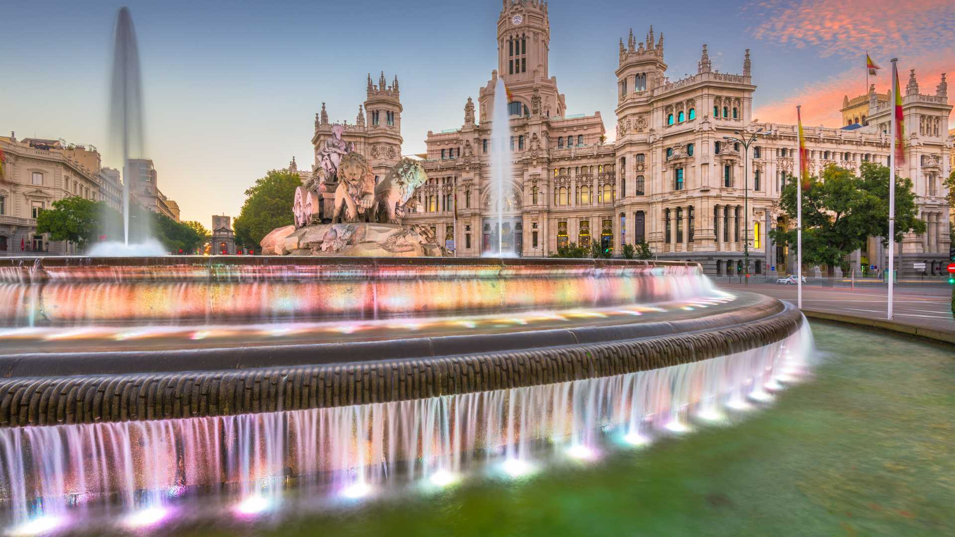 Levendige schemering op Plaza de Cibeles, Madrid, met verlichte fonteinen en het majestueuze Palacio de Cibeles.