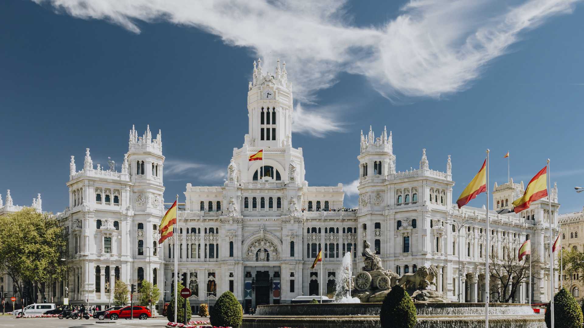 Het grandioze Palacio de Cibeles in Madrid, Spanje, onder een helderblauwe lucht, versierd met Spaanse vlaggen.