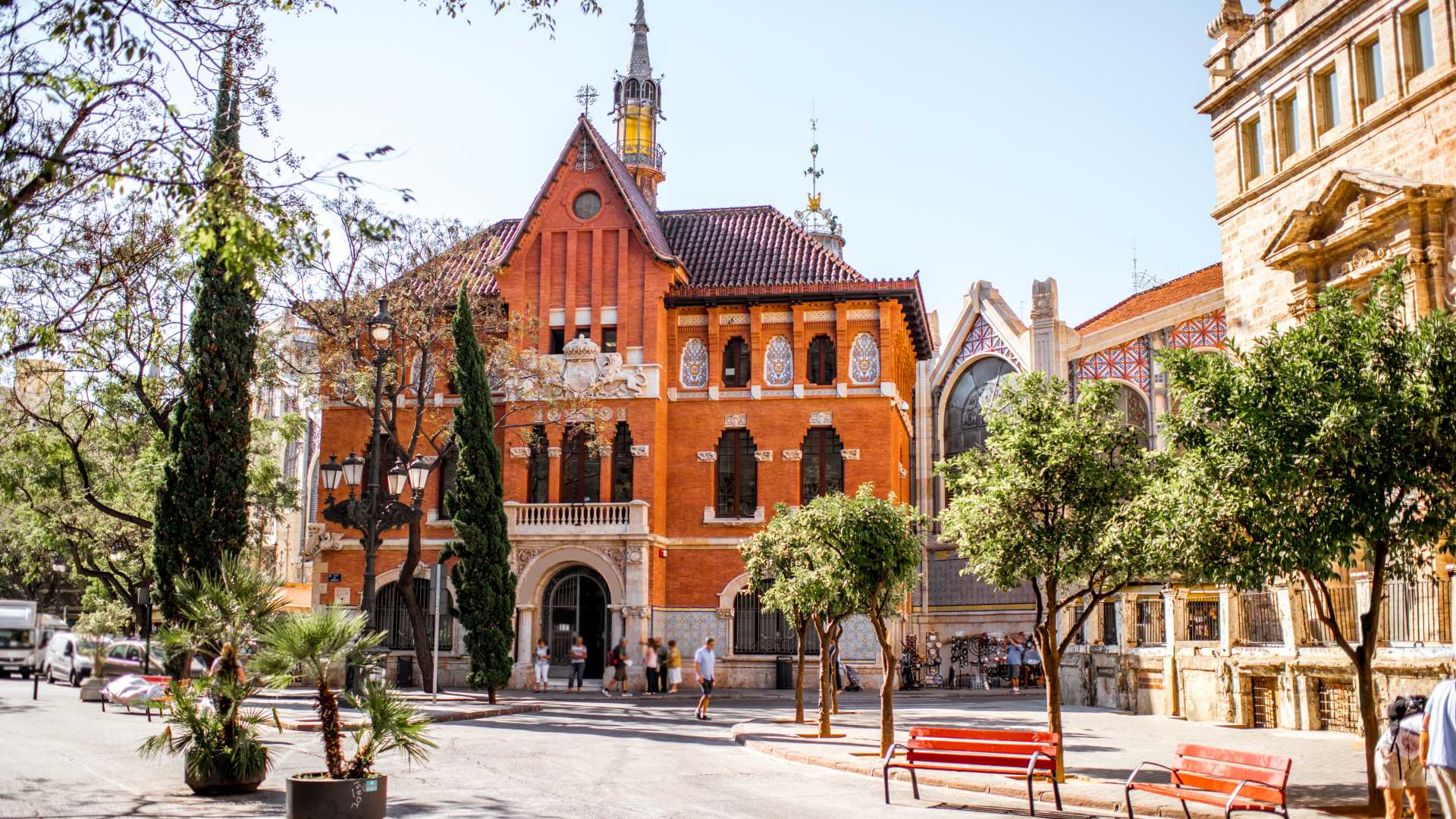 Charmant oud rood gebouw in de buurt van de centrale markt van Valencia, omgeven door bomen en levendige straatscènes.