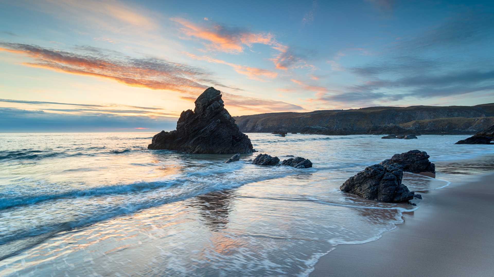 Zonsopgang boven Sango Bay in Durness, Schotland, met rotsen en zachte golven op het zandstrand.